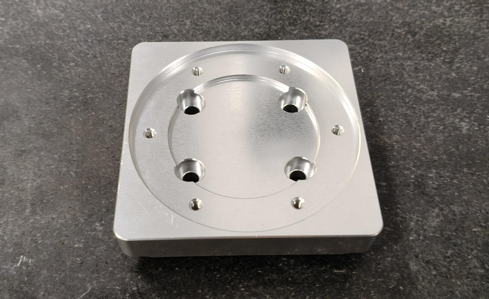 CNC machined aluminum part with a face milled flat surface, circular boss, and mounting holes